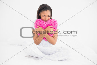 Peaceful young dark haired model cuddling a heart-shaped pillow