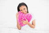 Amused young dark haired model cuddling a heart-shaped pillow