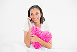 Pretty young dark haired model holding a pillow and making a phone call