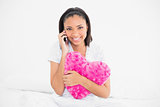 Smiling young dark haired model holding a pillow and making a phone call