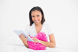 Pleased young dark haired model cuddling a pillow and using a tablet pc