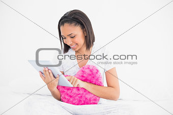Concentrated young dark haired model holding a pillow and using a tablet pc