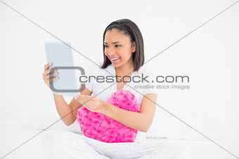 Concentrated young dark haired model cuddling a pillow and using a tablet pc