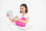 Content young dark haired model cuddling a pillow and using a tablet pc