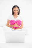 Smiling young dark haired model cuddling a pillow and using a laptop