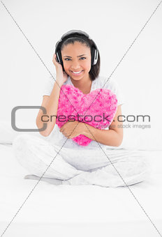 Calm young dark haired model cuddling a pillow and listening to music