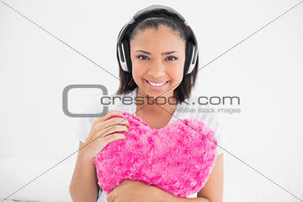 Joyful young dark haired model cuddling a pillow and listening to music