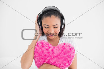 Relaxed young dark haired model cuddling a pillow and listening to music