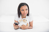 Thoughtful young dark haired model holding a mobile phone and a plush sheep
