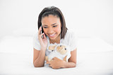 Cheerful young dark haired model making phone call while cuddling a plush sheep