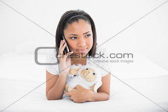 Dreamy young dark haired model making phone call while cuddling a plush sheep