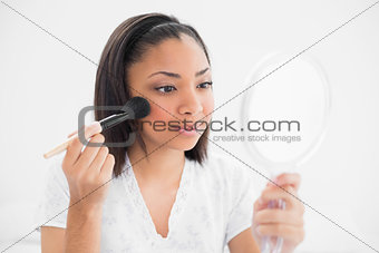 Attentive young dark haired model applying powder on her face