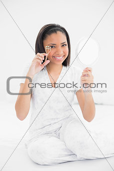 Happy young dark haired model using eyelash curler