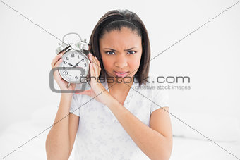 Frowning young dark haired model holding an alarm clock