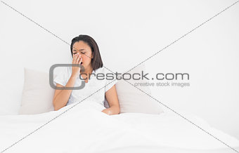 Exhausted young dark haired model yawning lying in her bed