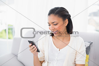 Happy young dark haired woman in white clothes looking at her mobile phone