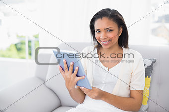 Pleased young dark haired woman in white clothes using a a tablet pc