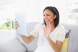 Joyful young dark haired woman in white clothes chatting with tablet pc