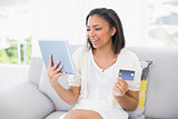 Delighted young dark haired woman in white clothes shopping online with a tablet pc
