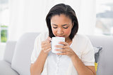 Peaceful young dark haired woman in white clothes enjoying coffee