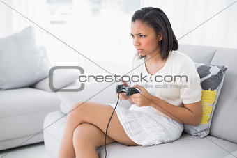 Frowning young dark haired woman in white clothes playing video games