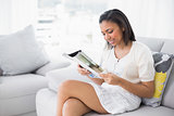 Concentrated young dark haired woman in white clothes reading magazines
