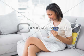 Delighted young dark haired woman in white clothes shopping online with a laptop