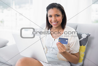 Pleased young dark haired woman in white clothes shopping online with a laptop