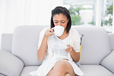 Relaxed young dark haired woman in white clothes enjoying coffee and cookies