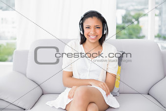 Smiling young dark haired woman in white clothes listening to music