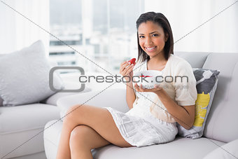 Delighted young dark haired woman in white clothes eating strawberries