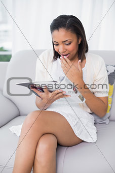Laughing young dark haired woman in white clothes reading a magazine