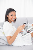 Smiling young dark haired woman in white clothes holding a magazine and a mobile phone