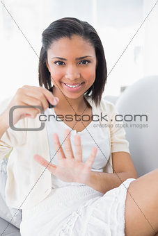 Beautiful young dark haired woman in white clothes applying nail polish