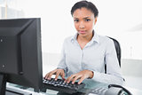 Stern young dark haired businesswoman typing on the computer