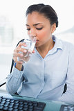 Calm young dark haired businesswoman drinking water
