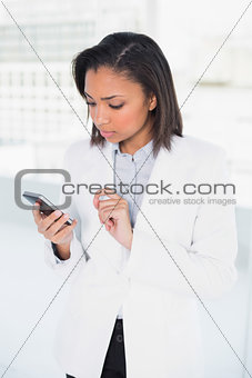 Thinking young dark haired businesswoman looking at her mobile phone