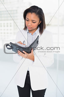 Thoughtful young dark haired businesswoman taking notes on her schedule