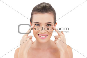 Smiling natural brown haired model pointing her eyes with her fingers