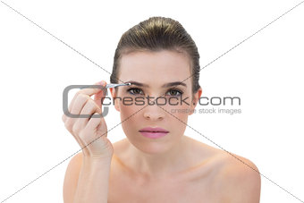 Concentrated natural brown haired model plucking her eyebrows