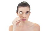 Pouting natural brown haired model using an eyelash curler