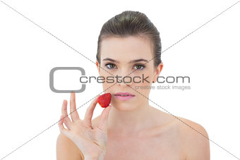 Serious natural brown haired model holding a strawberry