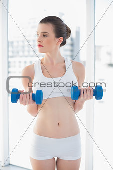 Thoughtful fit brown haired model in sportswear exercising with dumbbells