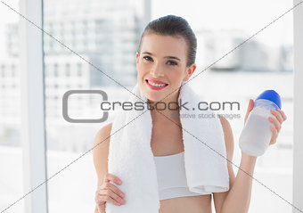 Cheerful fit brown haired model in sportswear carrying a bottle and a towel