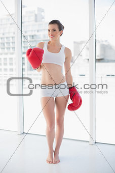 Pleased fit brown haired model in sportswear wearing red boxing gloves
