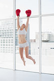 Cheerful fit brown haired model in sportswear jumping and wearing red boxing gloves