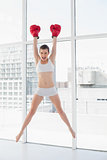 Confident fit brown haired model in sportswear jumping and wearing boxing gloves