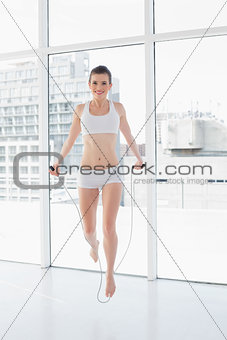 Pleased fit brown haired model in sportswear using a skipping rope