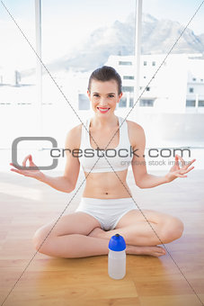 Happy fit brown haired model in sportswear meditating in lotus position