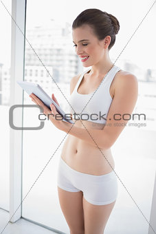Delighted fit brown haired model in sportswear looking at a tablet pc